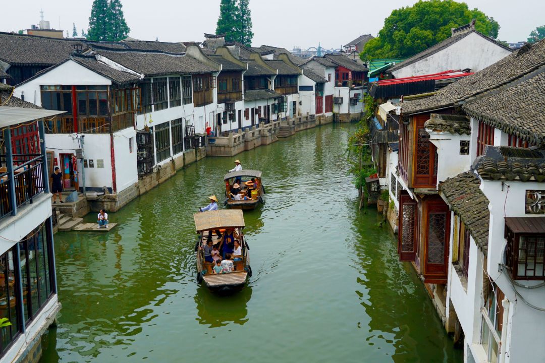 Zu sehen sind zwei Boote auf einem kleinen Flu&szlig; inmitten einer chinesischen H&auml;usersiedlung.